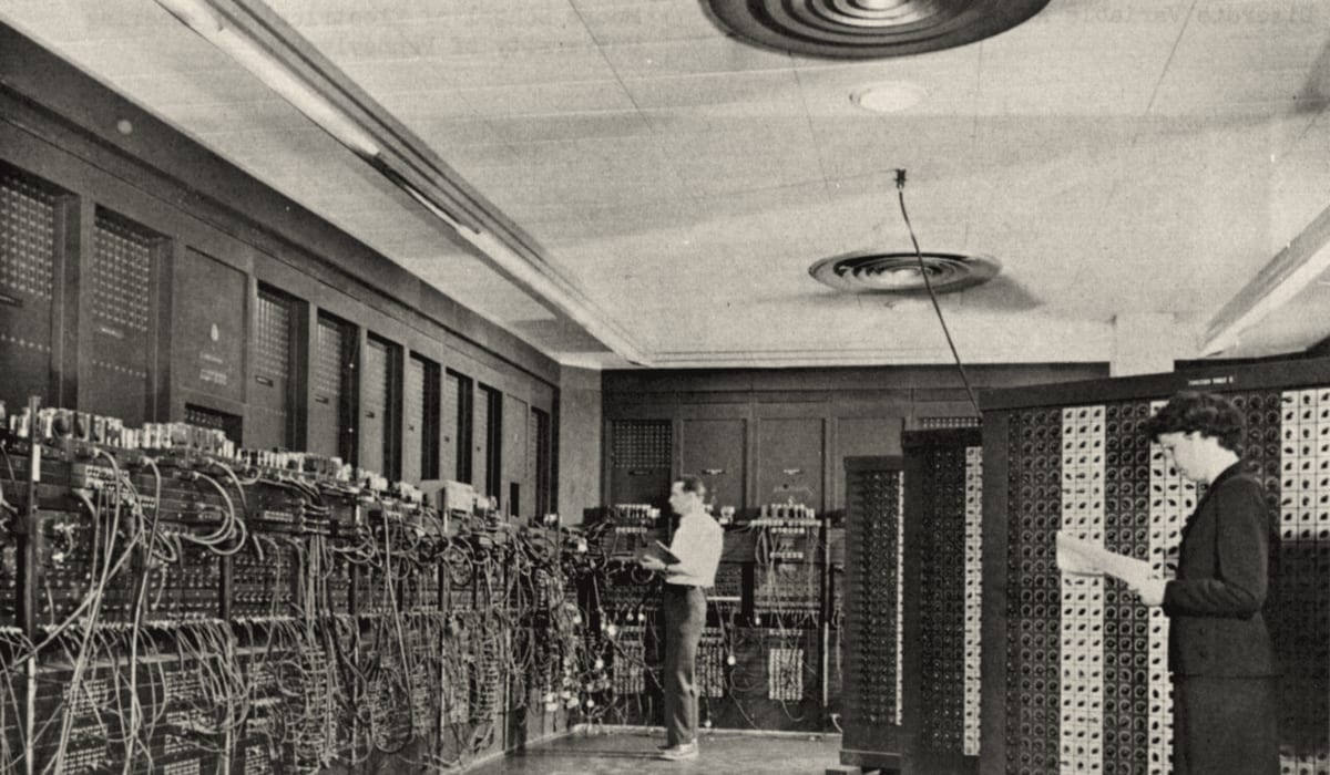Two people programming the ENIAC, a room-sized computer of cabinets, cables and switch panels.